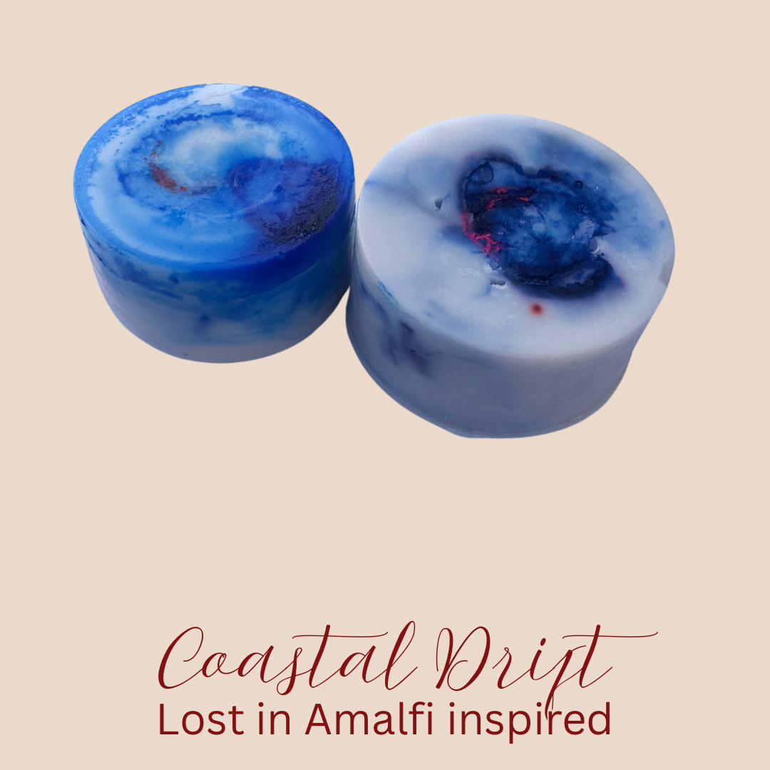 Two round blue and white marbled wax melts with embedded dark blue details, displayed on a beige background with the text 'Coastal Drift Lost in Amalfi inspired' below.