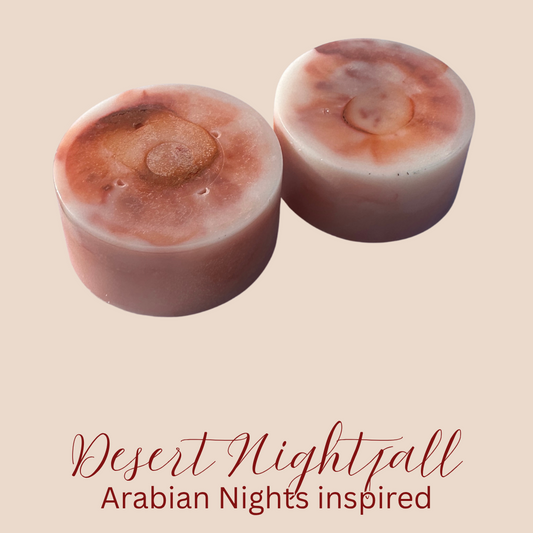 Two round, brownish beige wax melts with a marbled pattern, displayed on a solid beige background with the text 'Desert Nightfall Arabian Nights inspired' written below in red script.